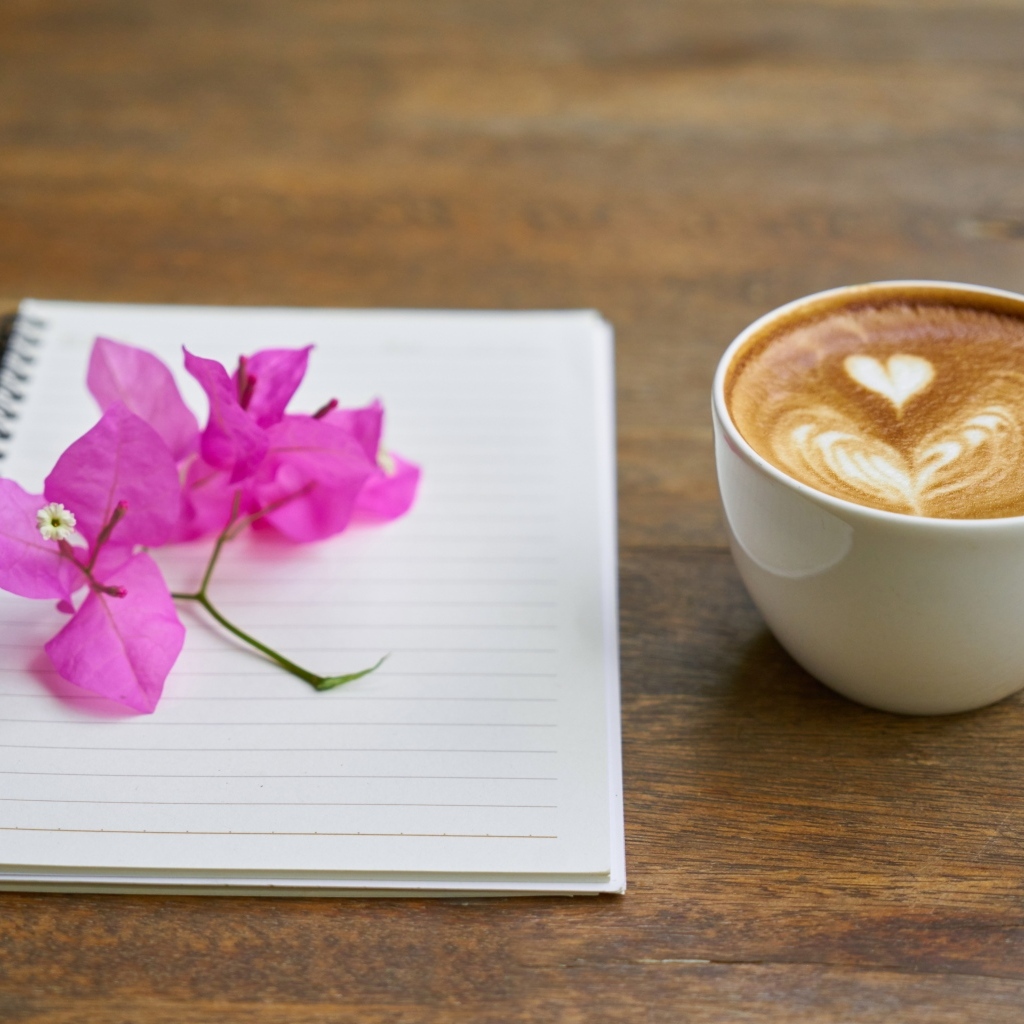 Чашка кофе на столе с блокнотом и цветами
