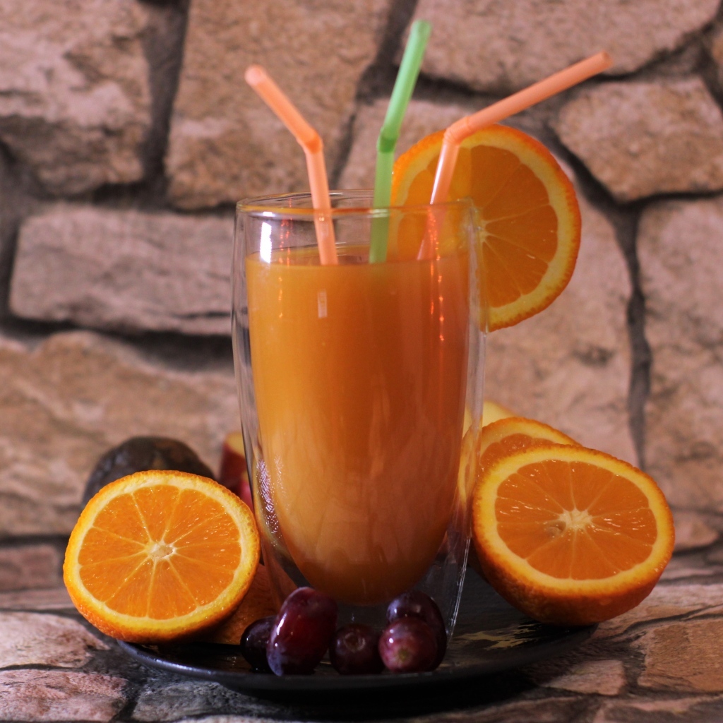 Стакан свежего сока с трубочками на столе с апельсинами