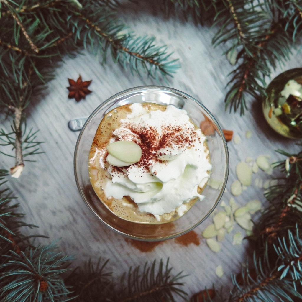 Горячий кофе с взбитыми сливками в чашке на столе с еловыми ветками