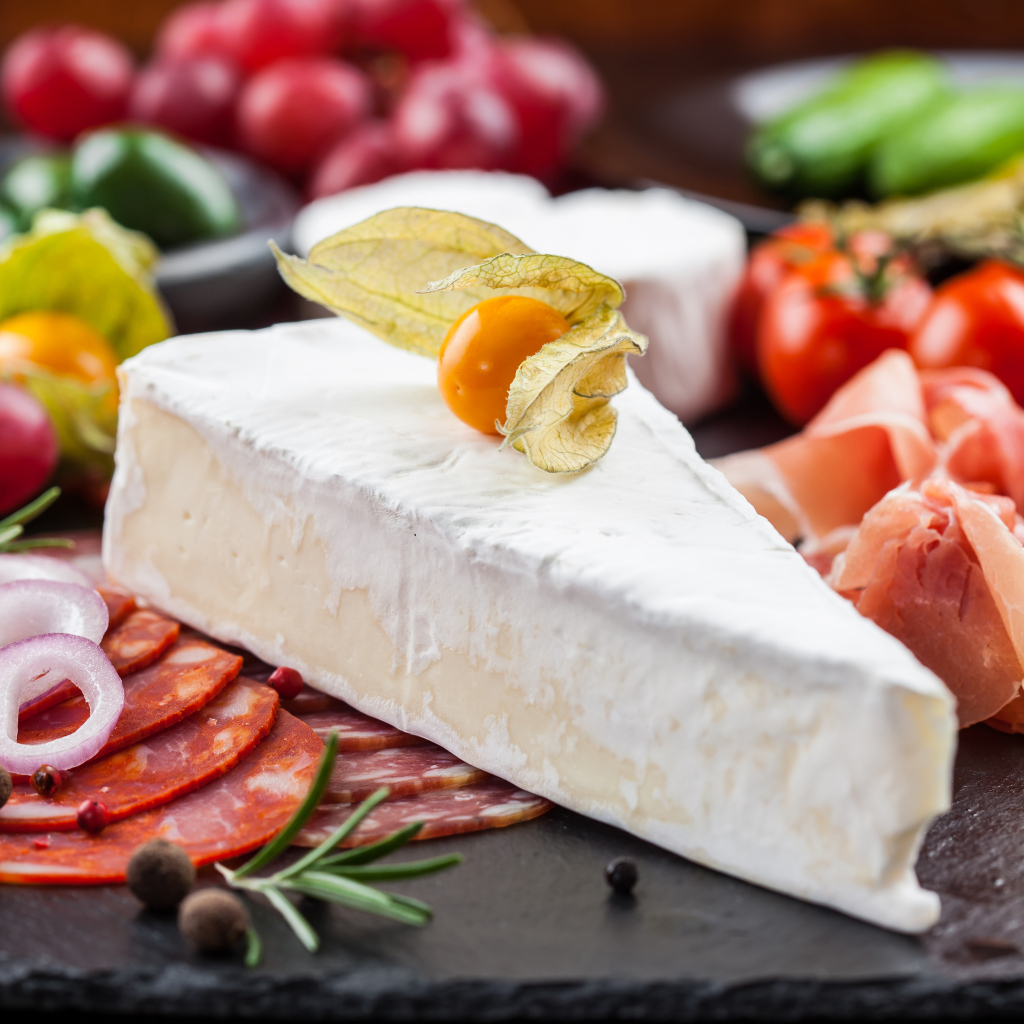 Кусок сыра на столе с овощами и колбасой
