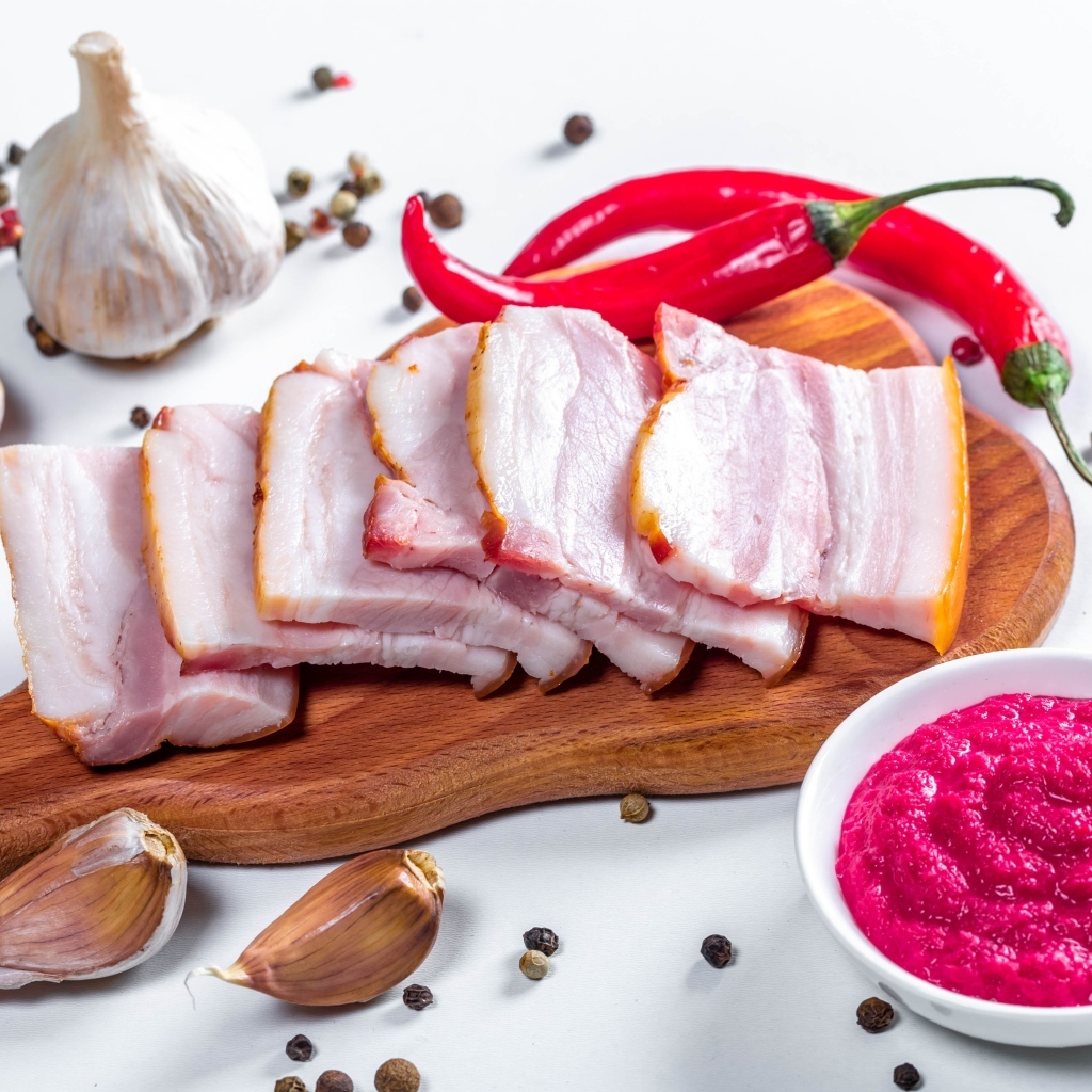 Нарезанное сало на столе с чесноком, хреном и красным перцем