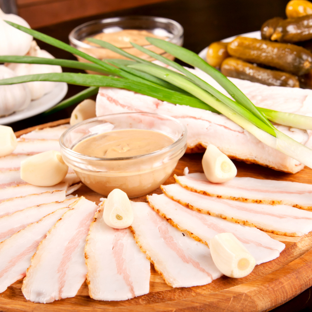 Нарезанное сало с чесноком и солеными огурцами на столе