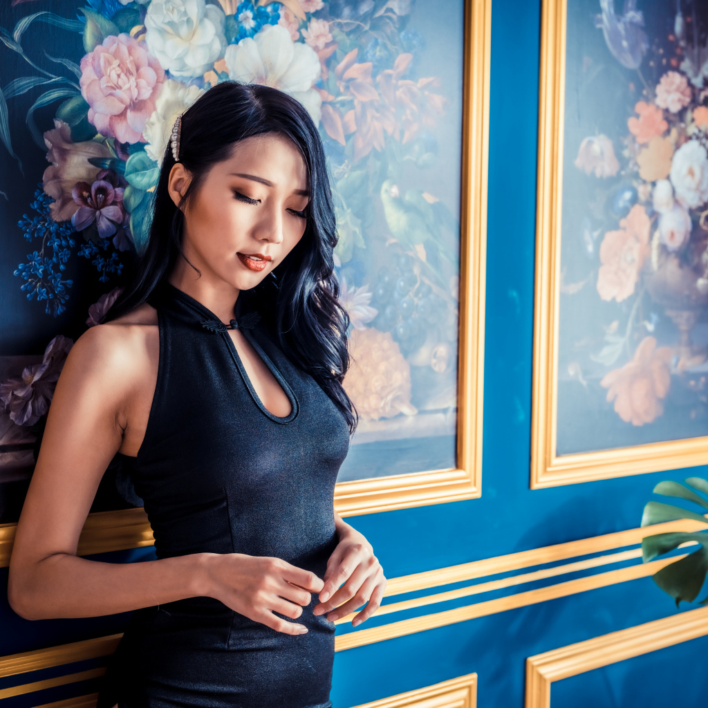 Красивая девушка азиатка в черном платье стоит у картины 