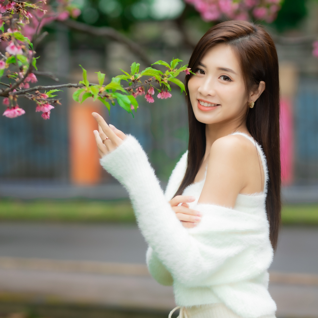 Красивая азиатка в белом свитере стоит у ветки дерева