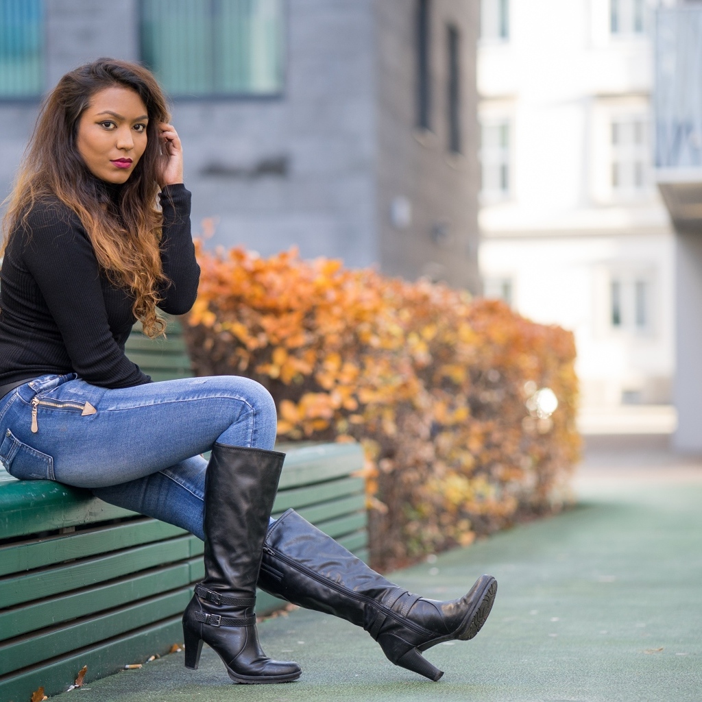 Брюнетка в синих джинсах сидит на лавке
