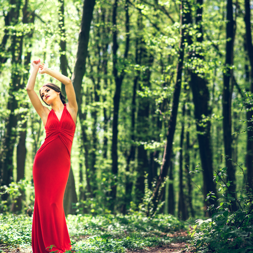 Девушка в красивом красном платье стоит в лесу