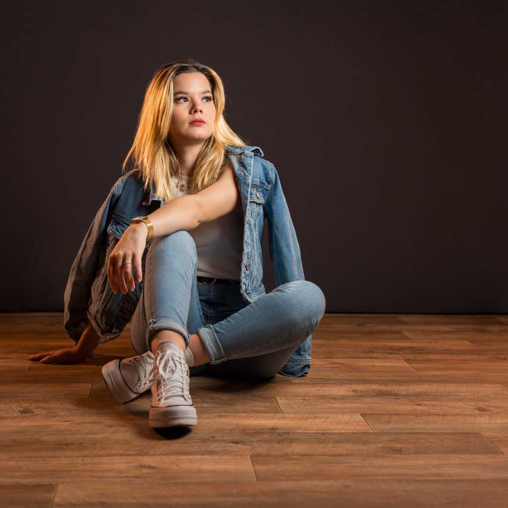 Девушка в джинсовом костюме сидит на полу