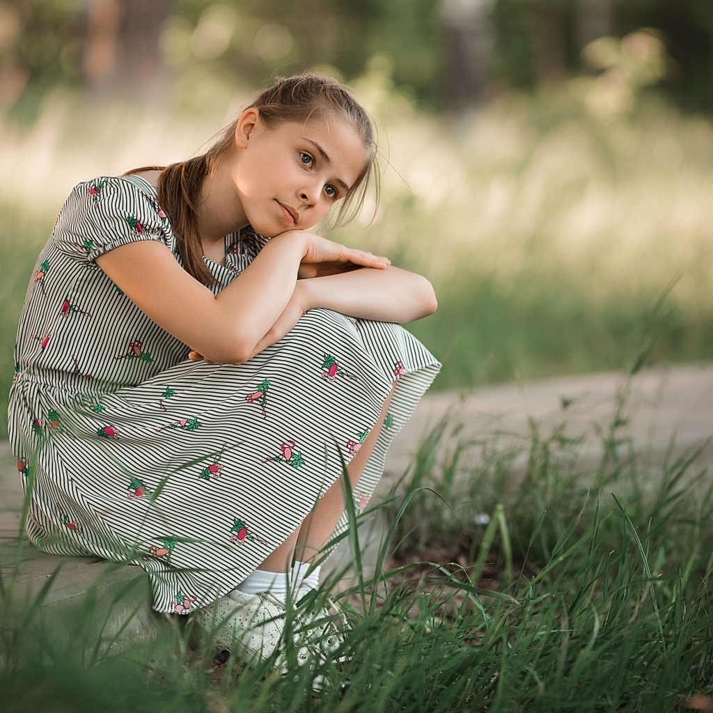 Девушка в платье сидит у зеленой травы