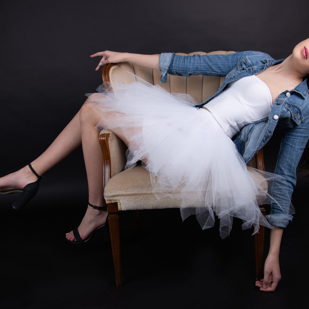 Девушка в белой юбке лежит в кресле на черном фоне