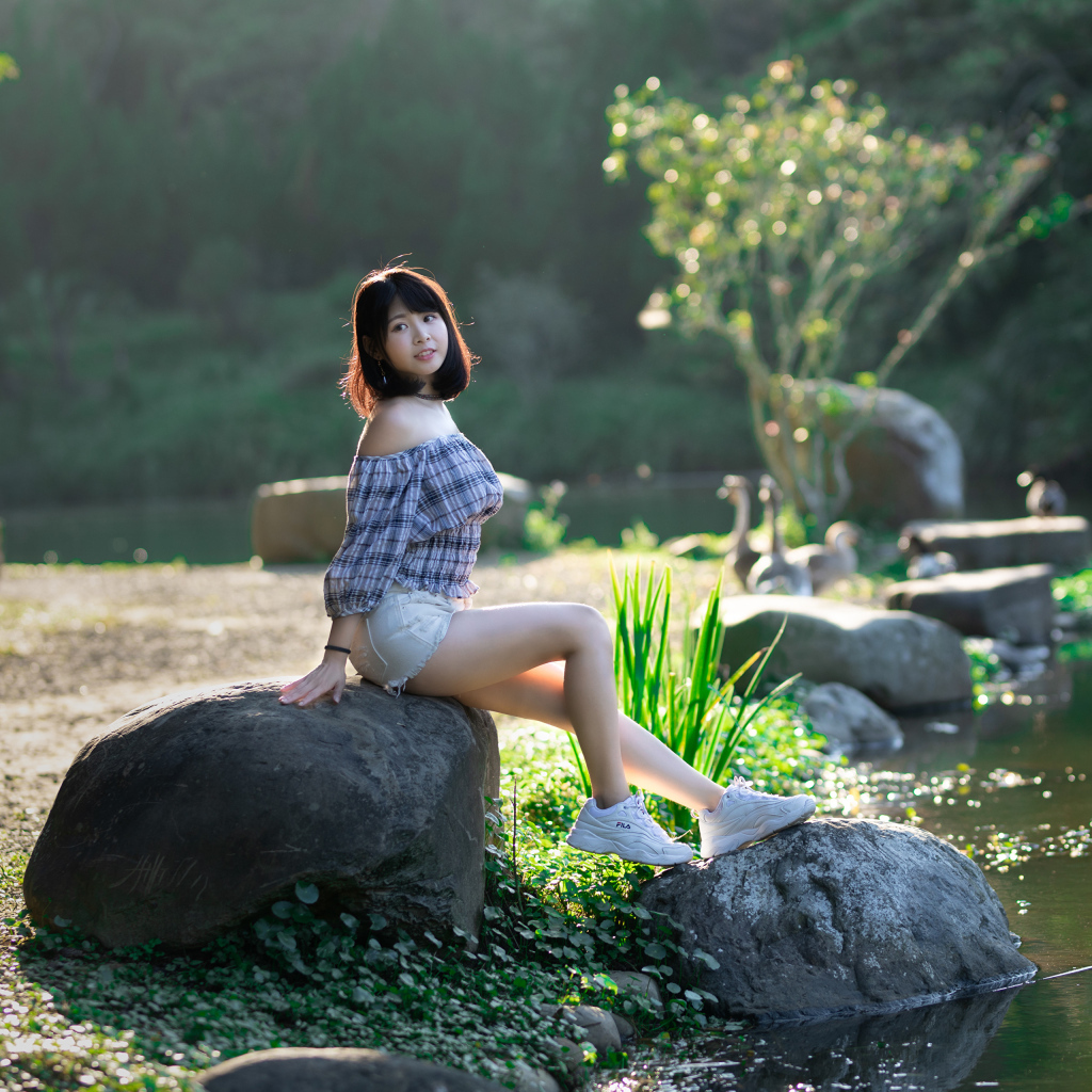 Девушка сидит на большом камне у пруда