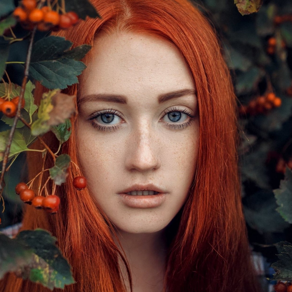 Рыжеволосая девушка стоит у куста с боярышником