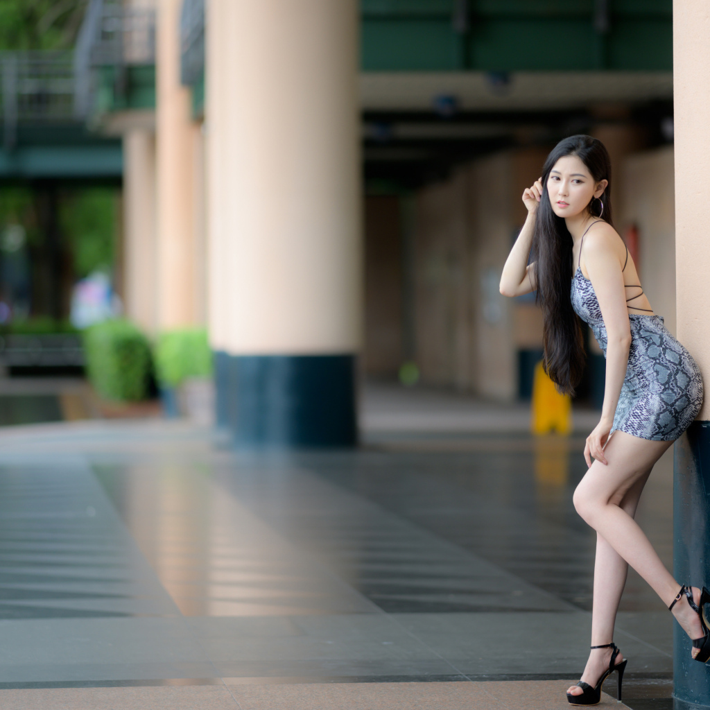 Стройная азиатка в коротком платье  стоит у колонны