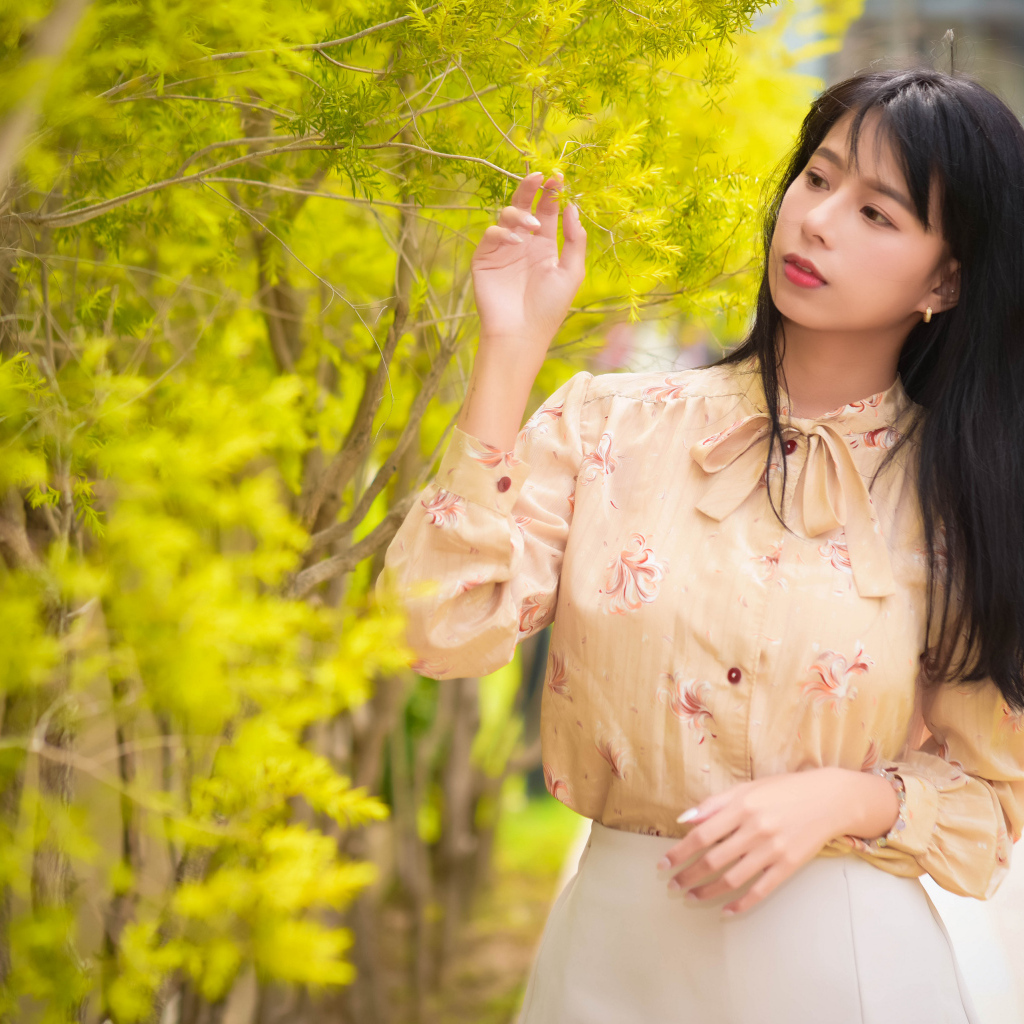 Молодая девушка азиатка стоит у дерева с зелеными листьями