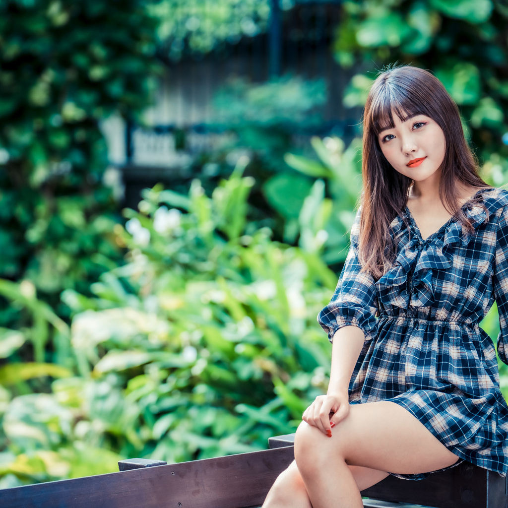 Молодая девушка в клетчатом платье сидит на заборе