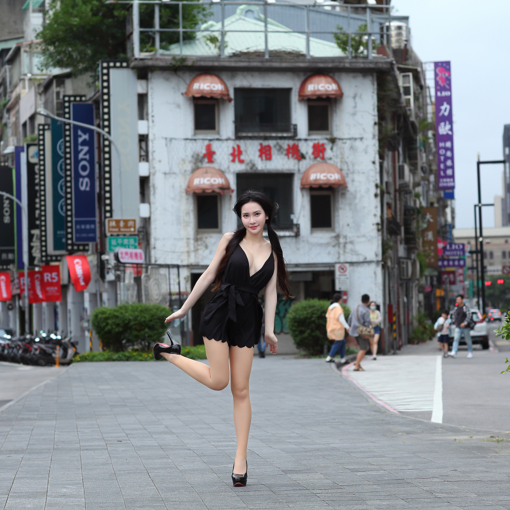 Девушка азиатка в черном платье стоит у дома