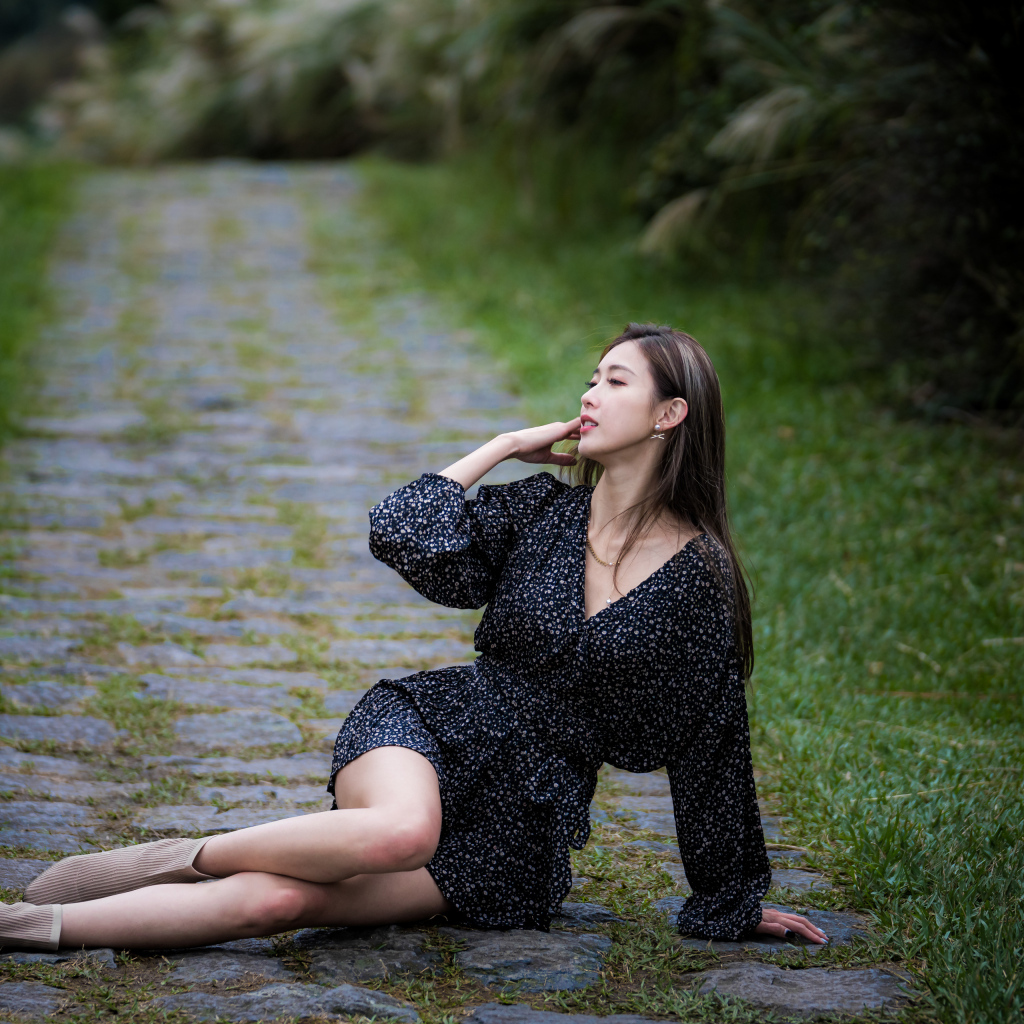 Девушка азиатка в платье лежит на дороге в парке