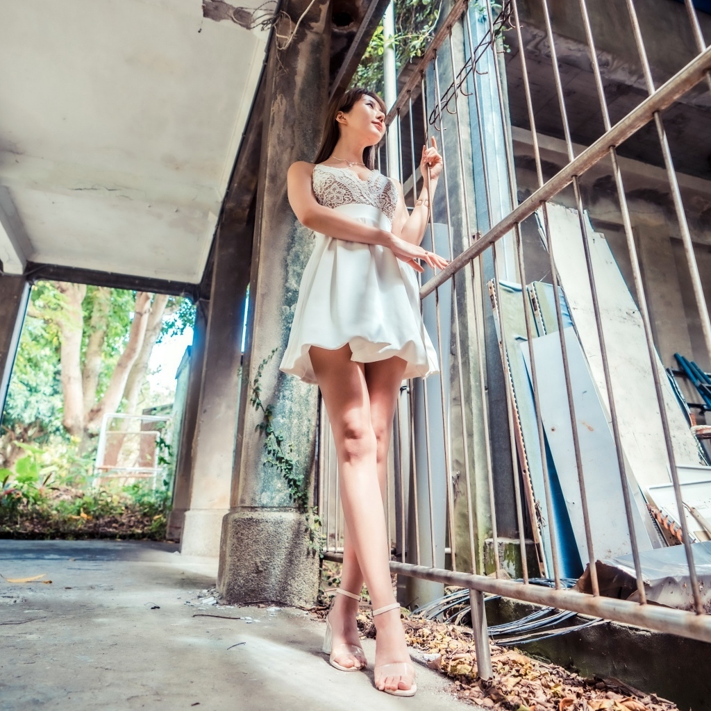 Девушка азиатка в платье стоит у решетки 