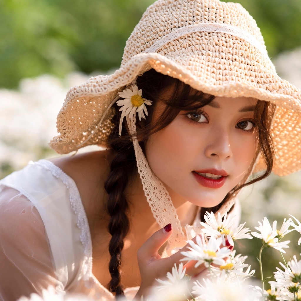 Девушка азиатка в шляпке на поле с ромашками