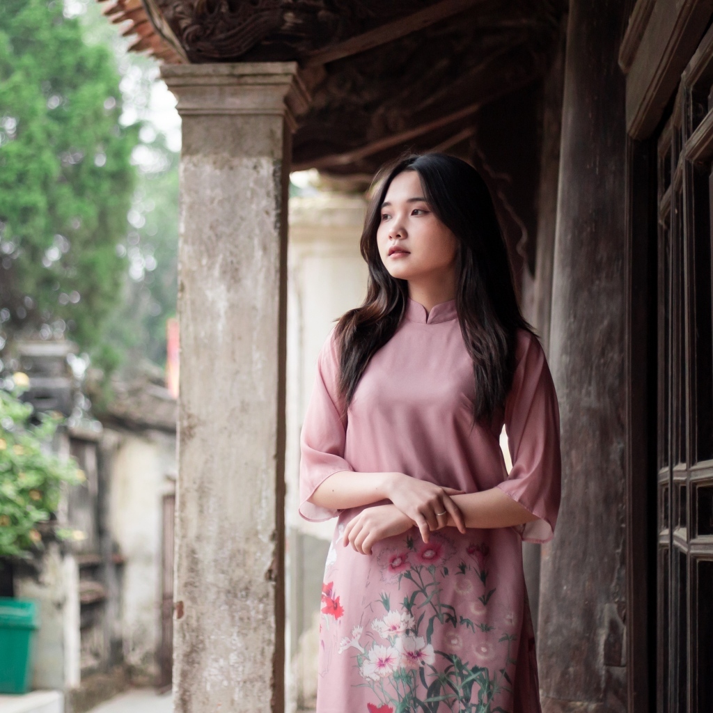 Девушка азиатка в розовом платье стоит у дома