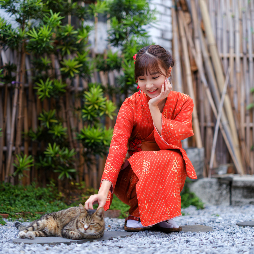 Девушка азиатка в красном платье гладит кота