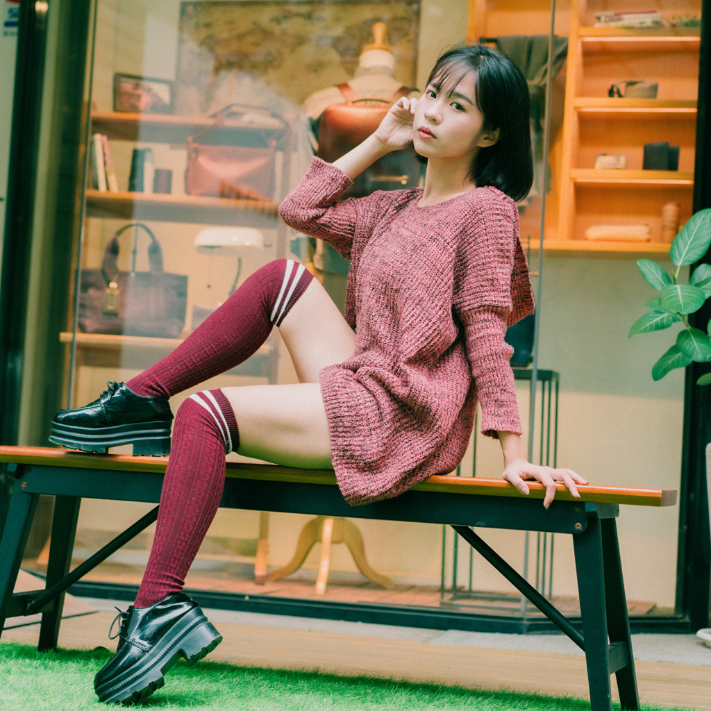 Девушка азиатка в теплом свитере сидит на лавке