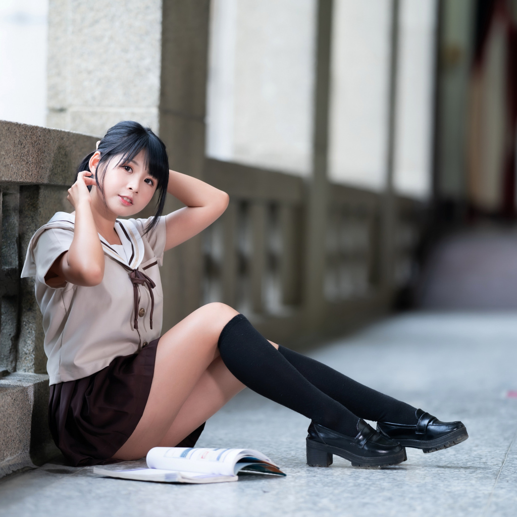 Девушка азиатка в школьной форме сидит на полу