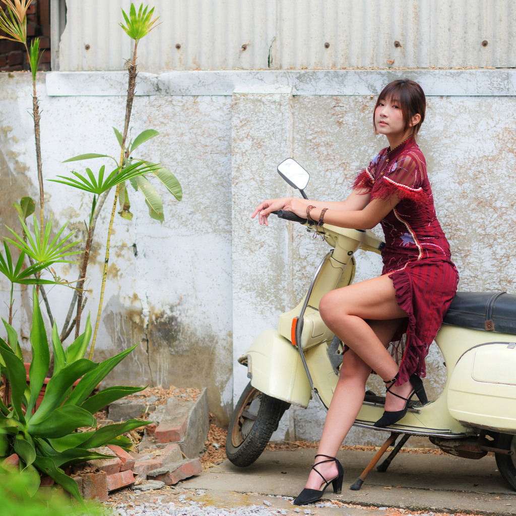 Девушка азиатка сидит на скутере у стены