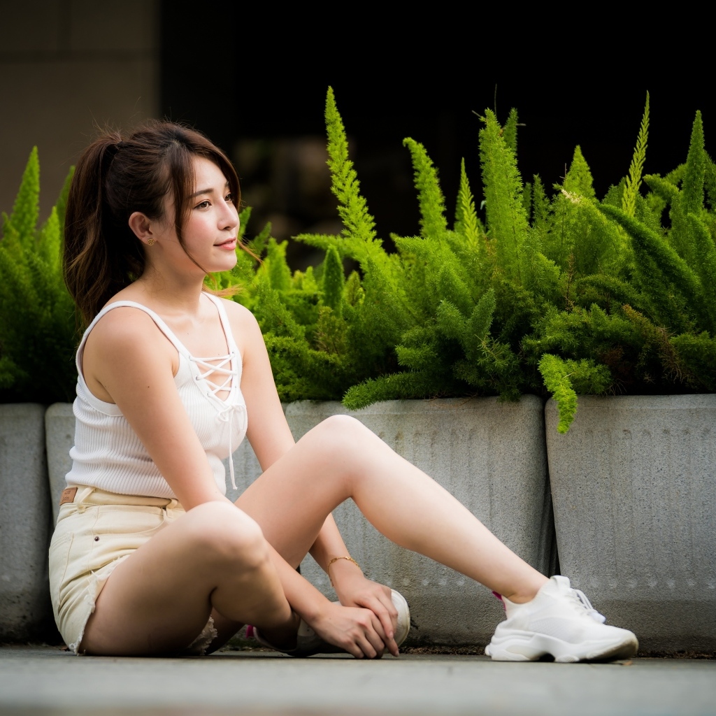 Девушка азиатка сидит на земле у зеленых растений