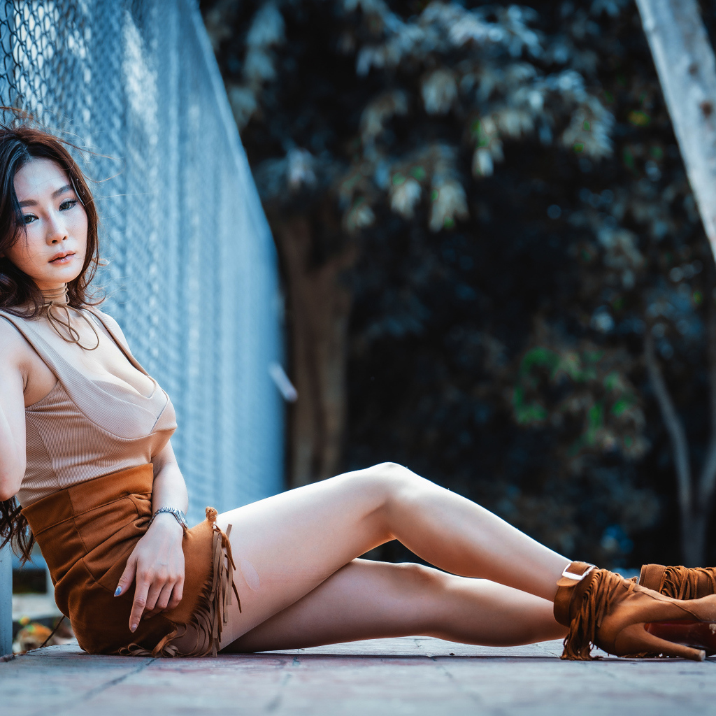 Девушка азиатка сидит на земле у сетки