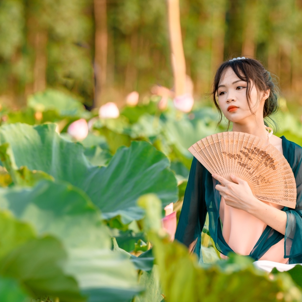 Девушка азиатка с веером в зеленых листьях лотоса