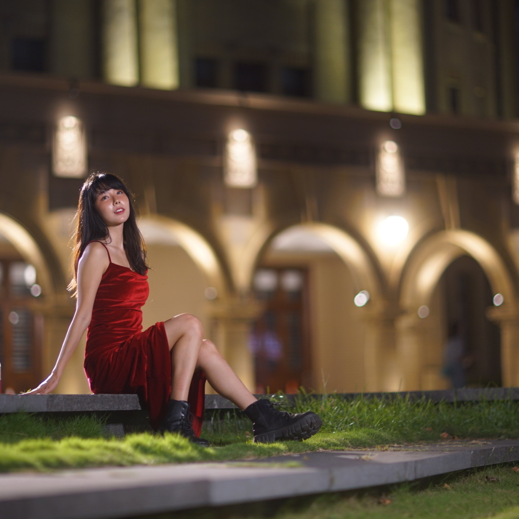 Азиатка в длинном красном платье сидит на ступенях