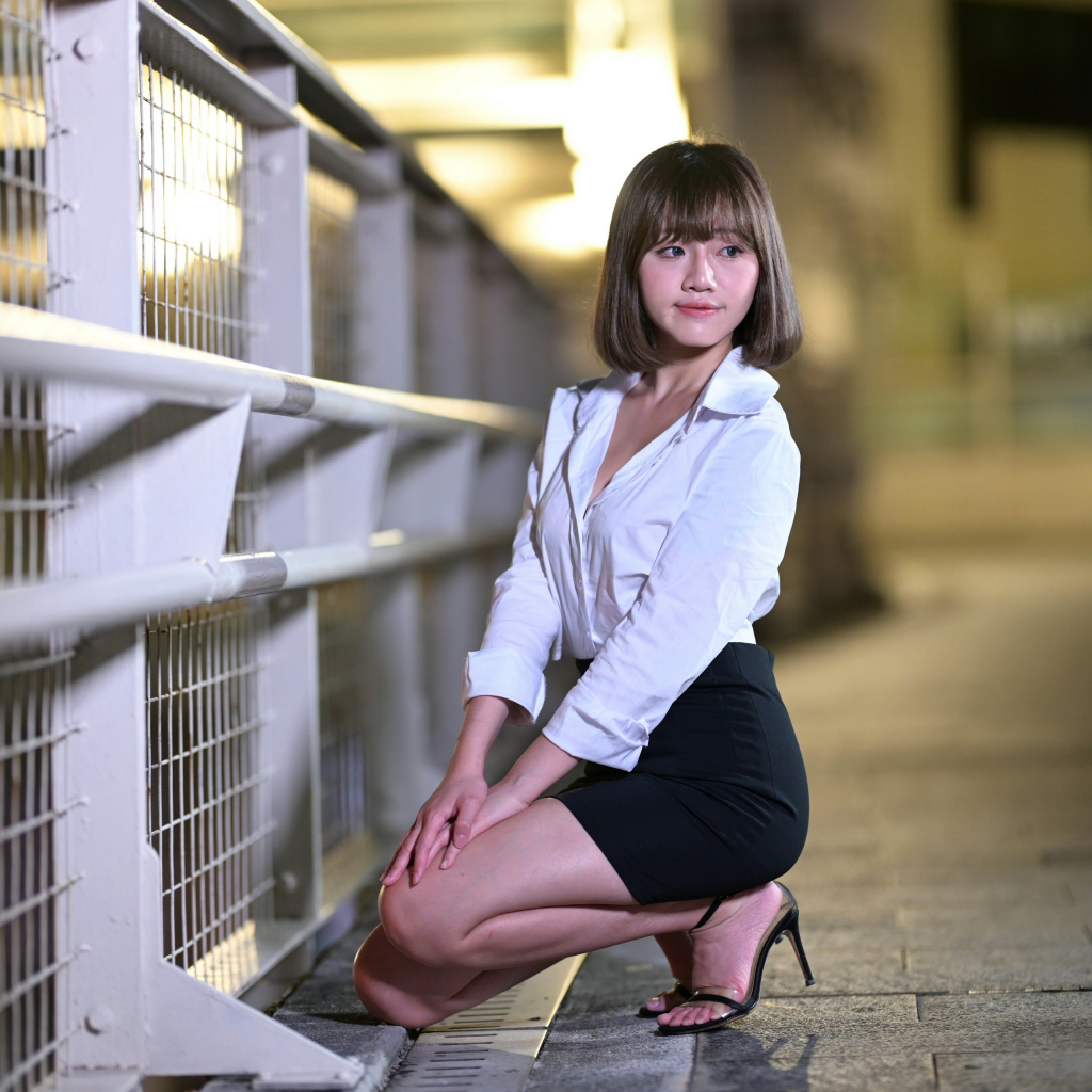 Азиатка в белой блузке и черной юбке сидит на корточках