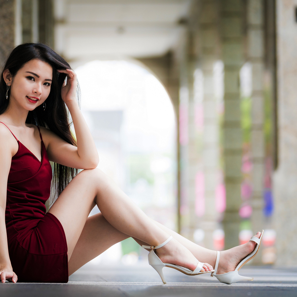 Азиатка в красном платье сидит у стены 