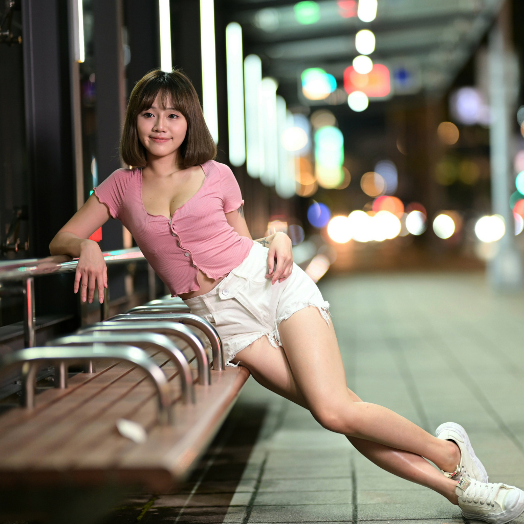 Азиатка в коротких белых шортах сидит на остановке