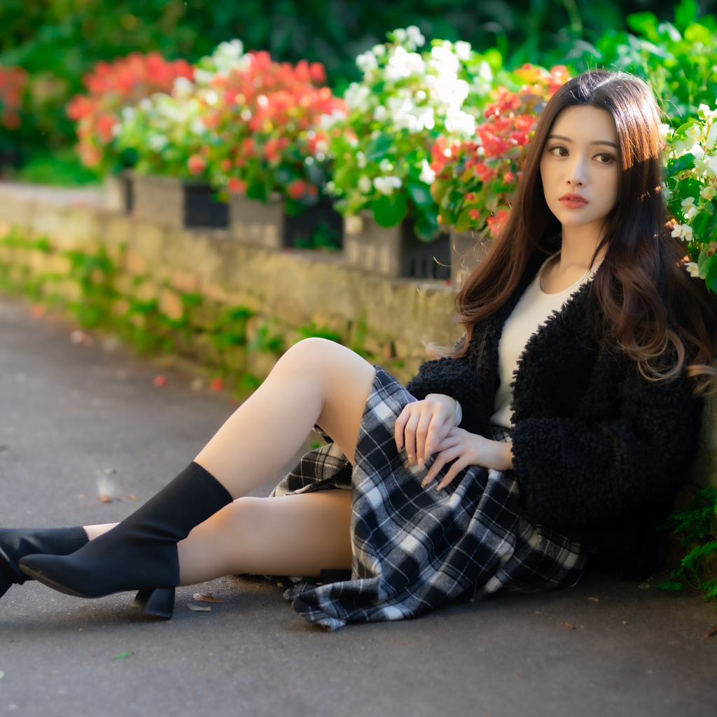 Азиатка сидит на асфальте у цветов