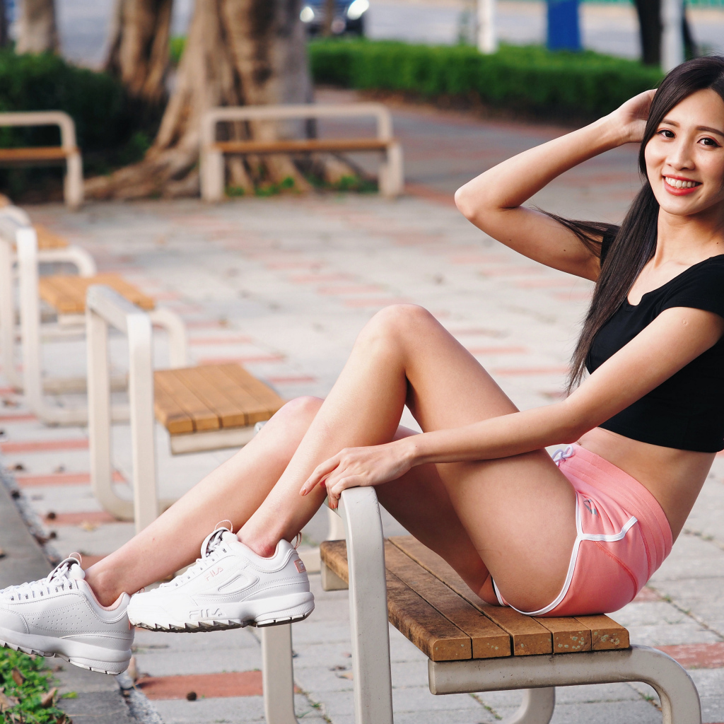 Спортивная девушка азиатка сидит на лавке 