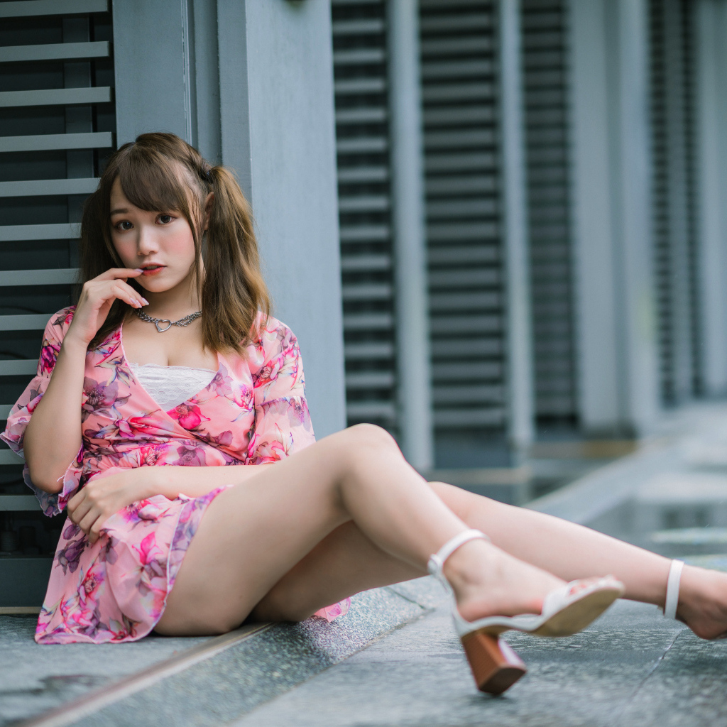 Красивая азиатка в розовом платье сидит у стены