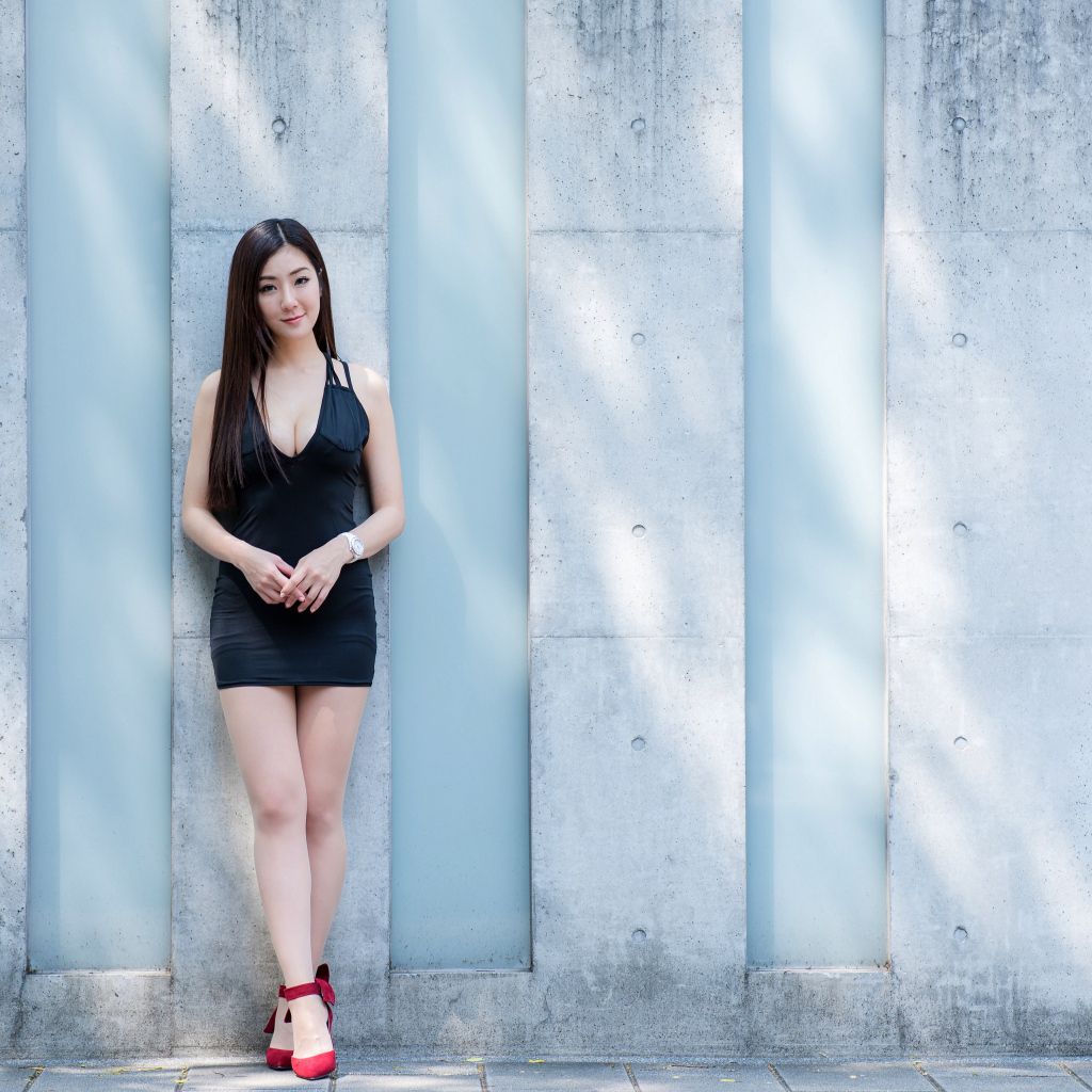 Красивая азиатка в коротком платье стоит у стены