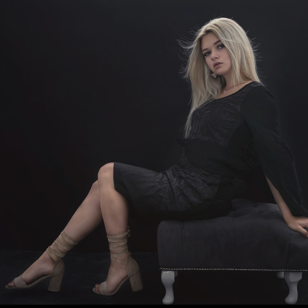 Красивая девушка в черном платье сидит на кресле
