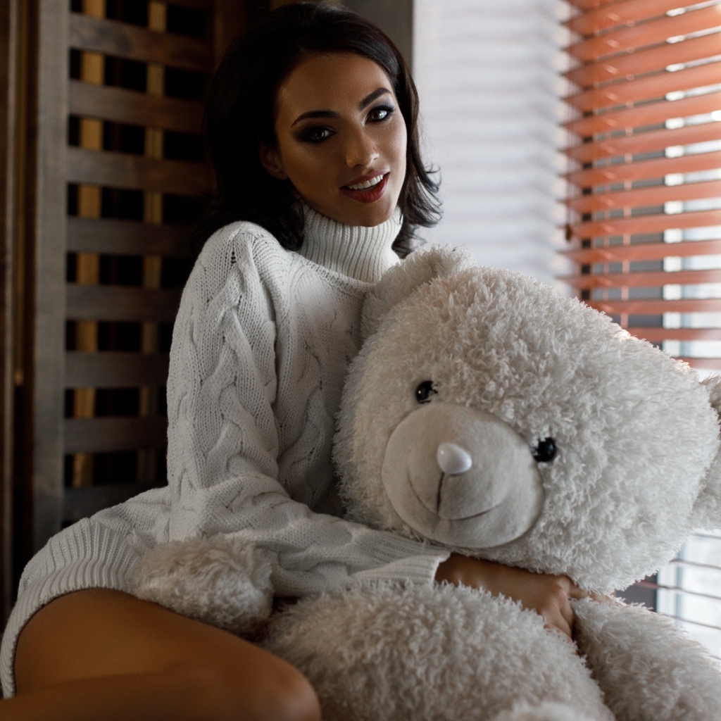 Красивая девушка в свитере с медведем у окна