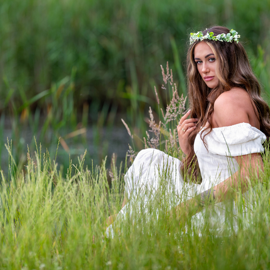 Красивая девушка в белом платье с венком на голове у пруда 