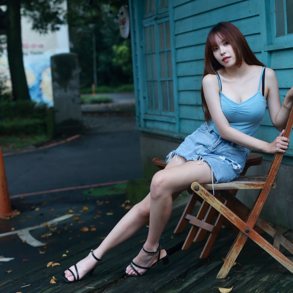 Красивая девушка сидит на стуле у дома