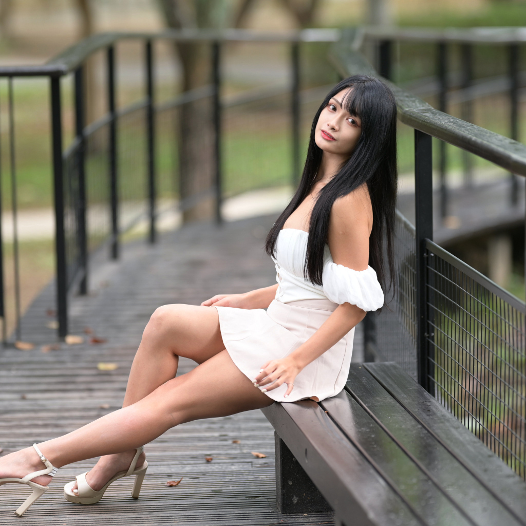 Красивая длинноволосая азиатка в белом платье сидит на лавке