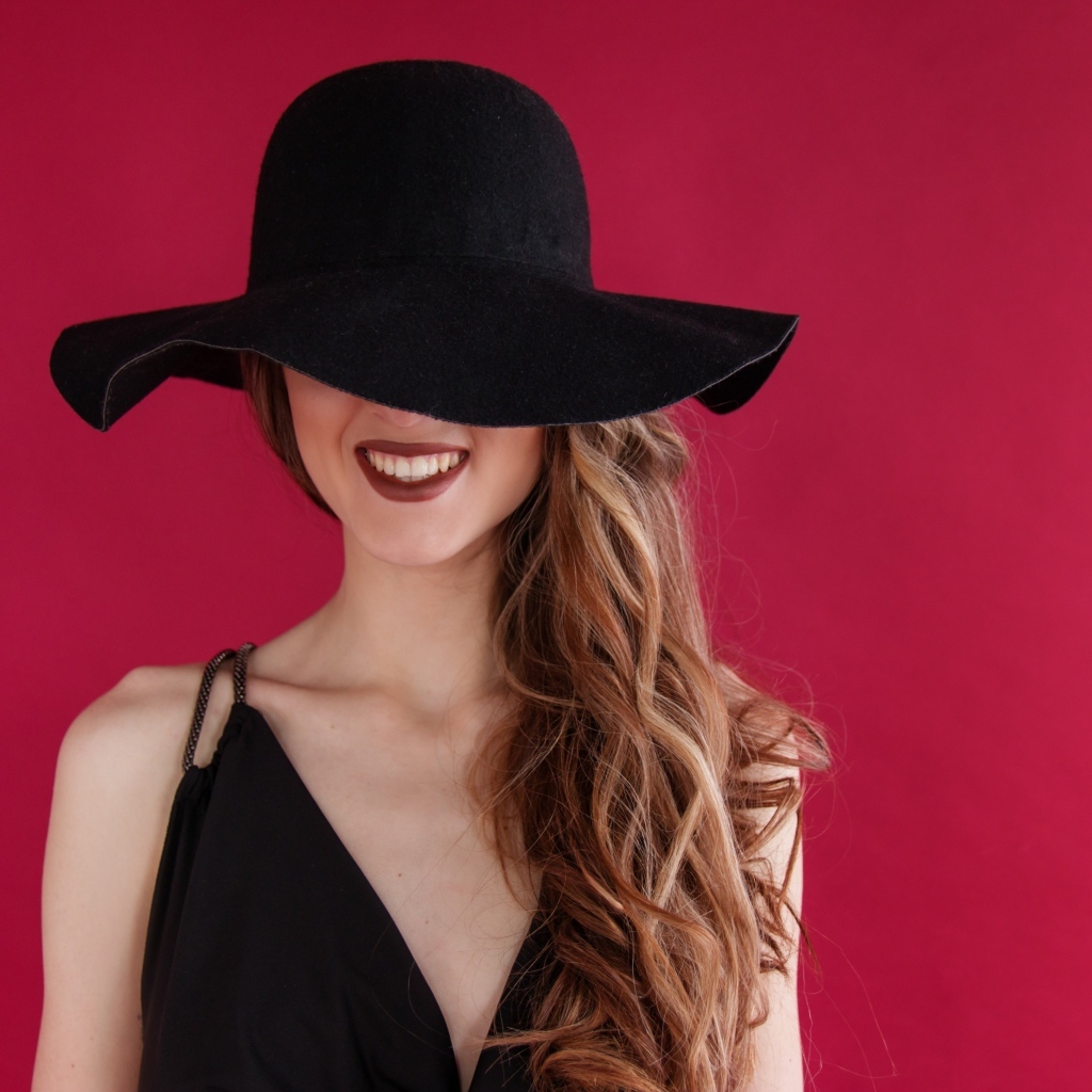 Черная шляпа на лице у девушки на розовом фоне