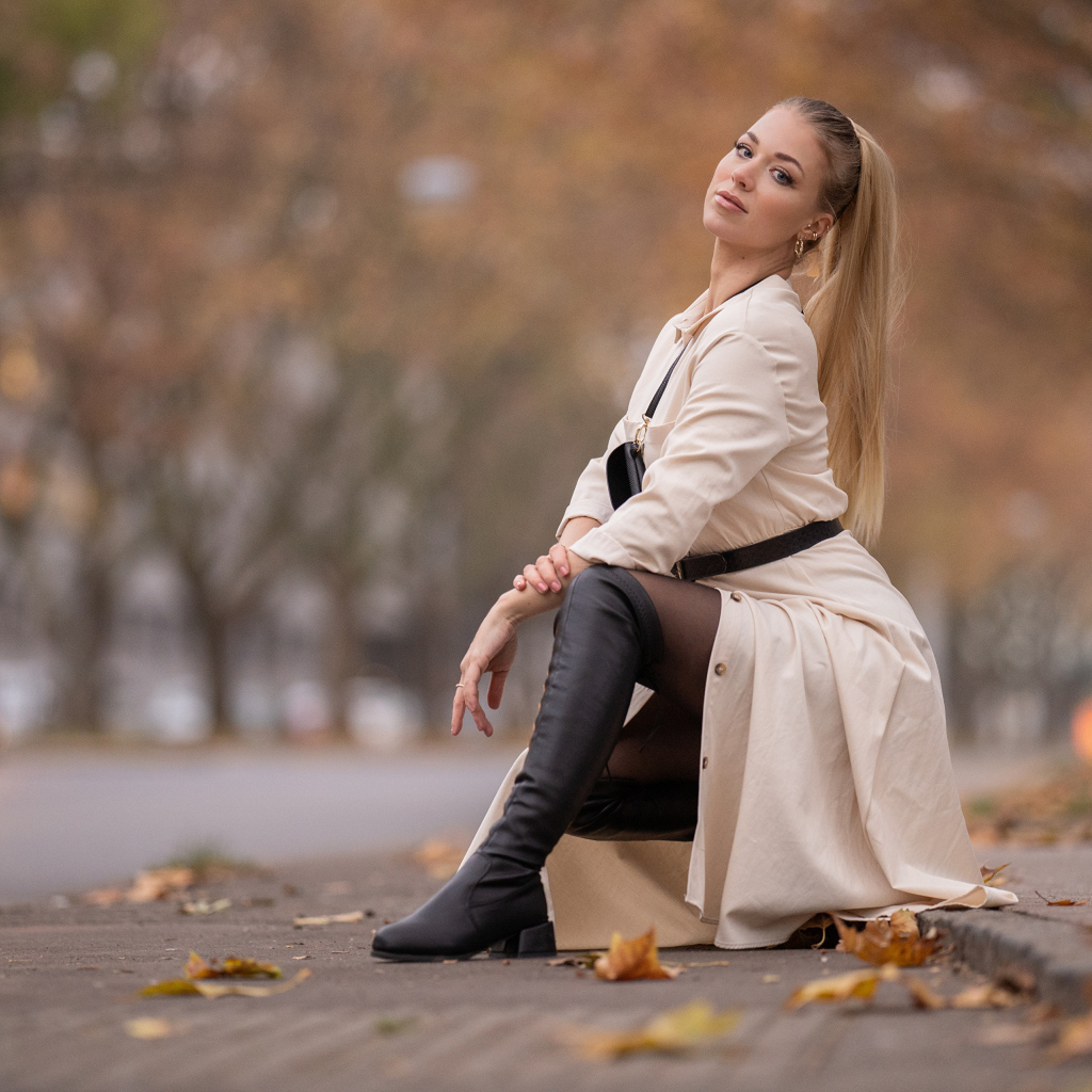 Девушка блондинка сидит в пальто в парке