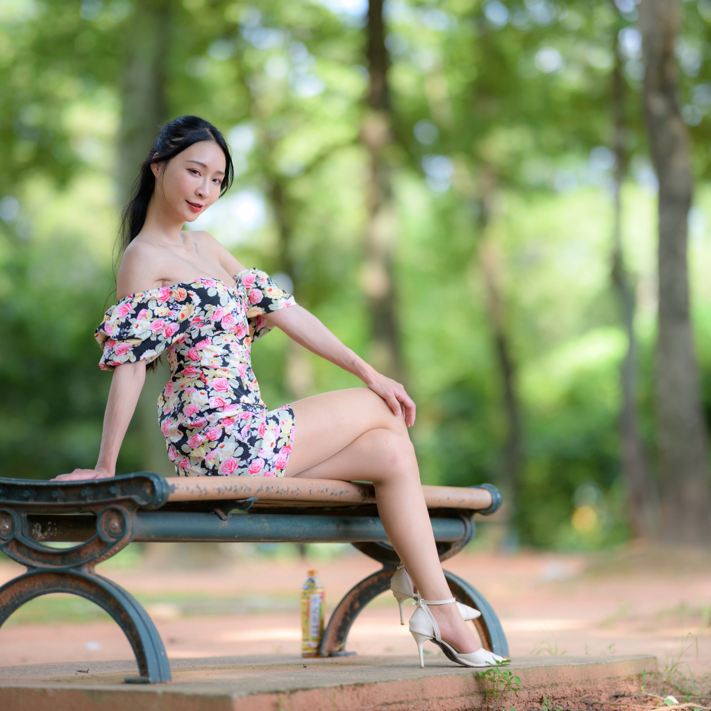 Милая девушка азиатка в платье сидит на лавке в парке