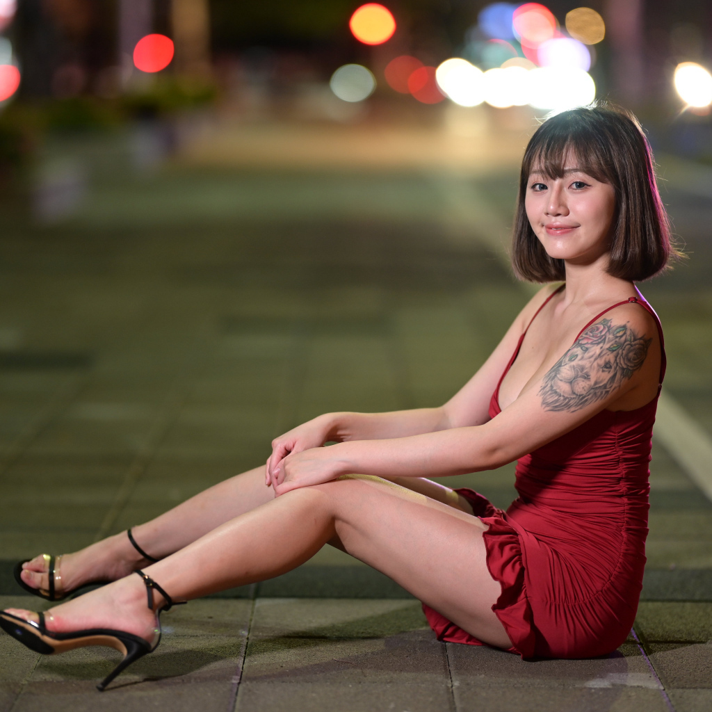 Милая азиатка в красном платье сидит на дороге