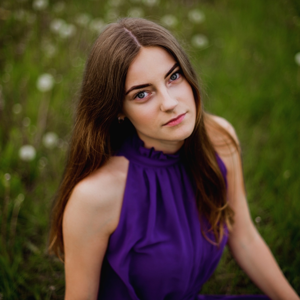 Милая девушка в фиолетовом платье сидит на траве