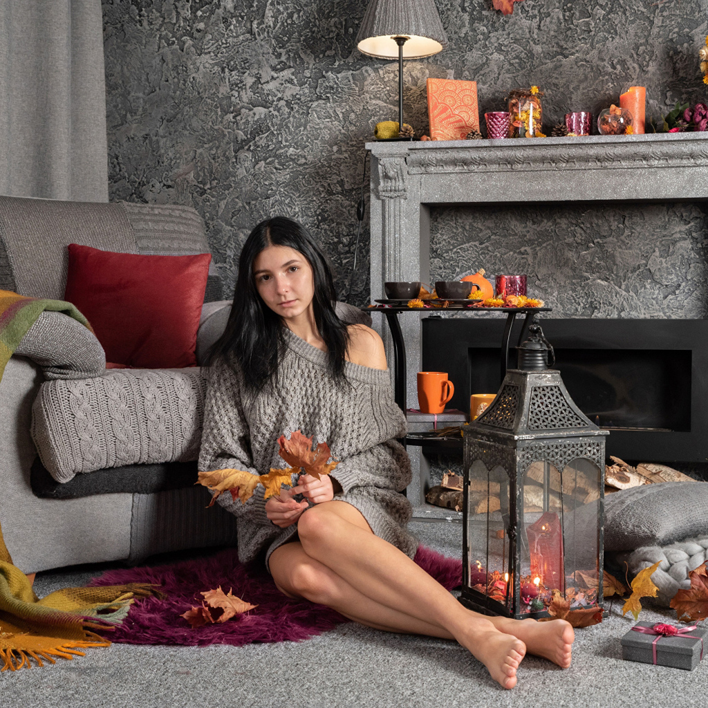 Милая девушка в теплом свитере сидит в комнате с камином