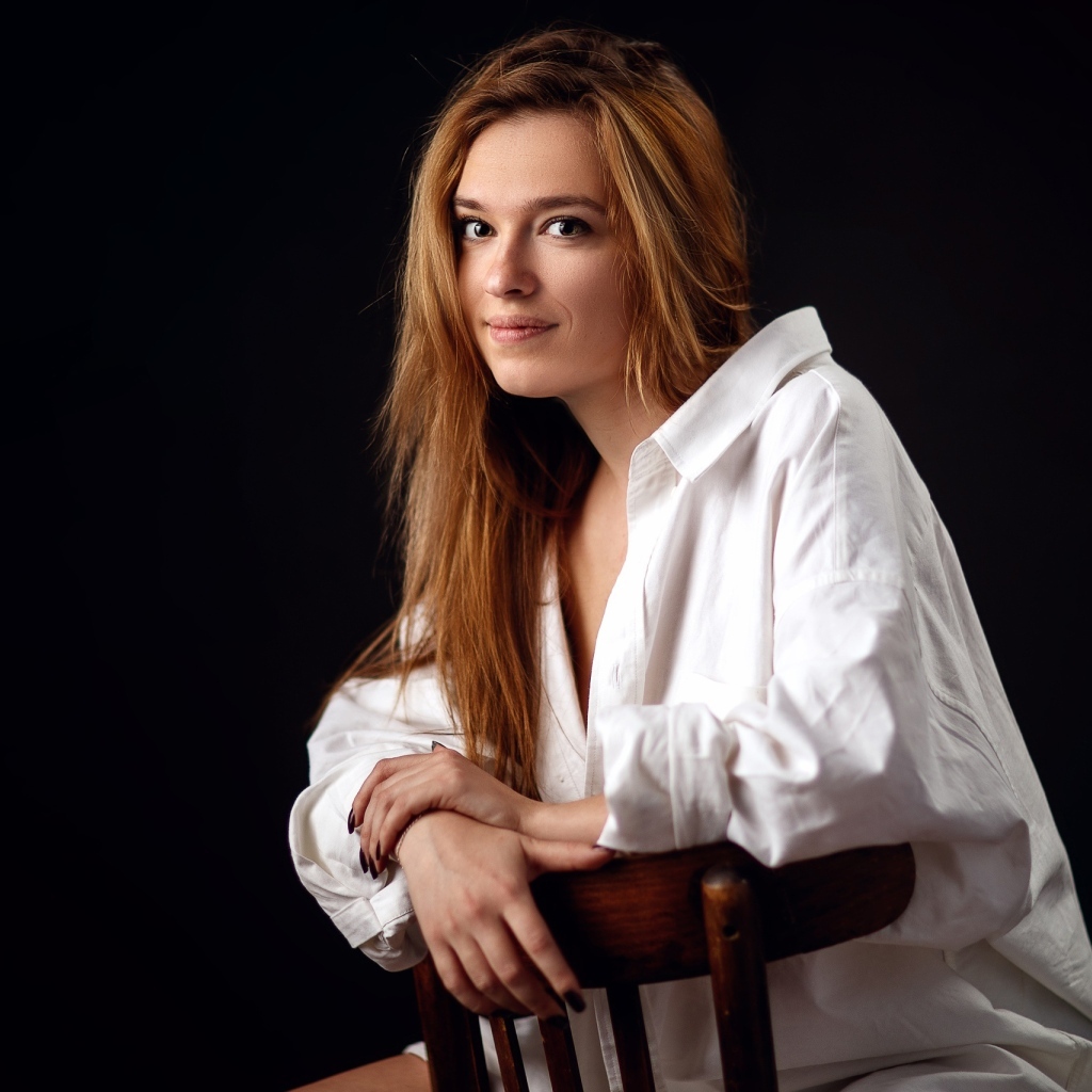 Милая девушка в белой рубашке сидит на стуле